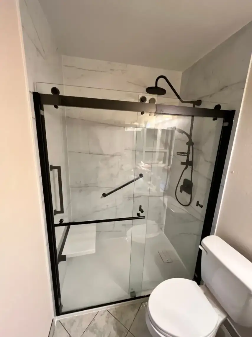 Modern walk-in shower with sliding glass doors, black matte hardware, and marble-patterned tile walls.